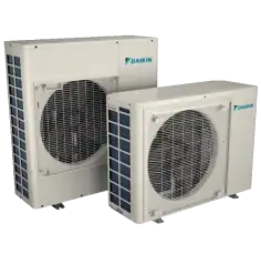 Two Daikin outdoor air conditioning units are placed side by side, showing front ventilation grills and brand logos on a plain, light background.